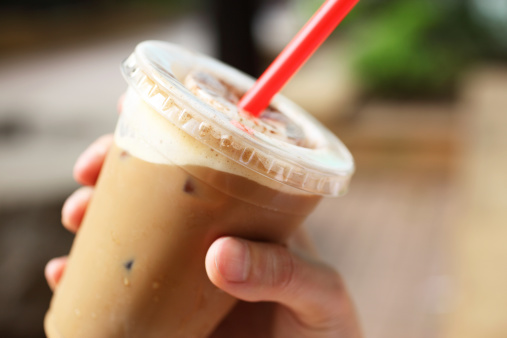 A cup of iced coffee in hand outdoors.