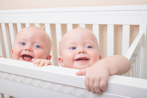 Identical Twin Baby Boys 9 month old identical twin boys standing up and laughing in their crib. twins stock pictures, royalty-free photos & images