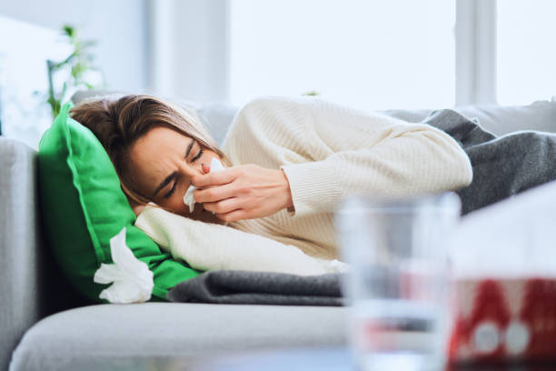 Ill woman sneezing her nose lying on the sofa at home stock photo