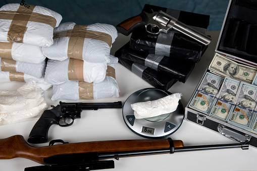 Confiscated illegal substance with measuring scale indicating 5 ounces, guns, and a briefcase full of American currency.