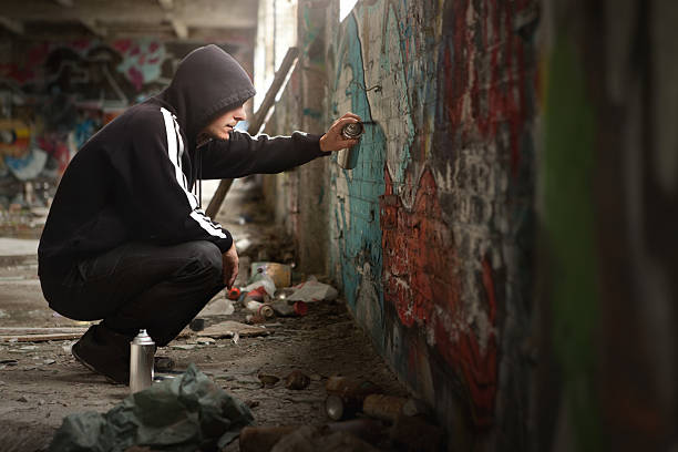 Illegal Young man Spraying paint on a Graffiti wall. Illegal Young man Spraying black paint on a Graffiti wall. (room for text) vandalism stock pictures, royalty-free photos & images