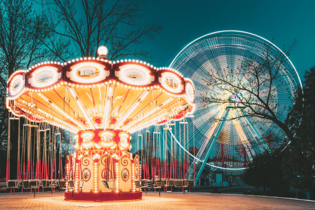 beleuchteter attraktions-riesenrad und karussell merry-goround on summer evening in city amusement park. - fahrgeschäft stock-fotos und bilder