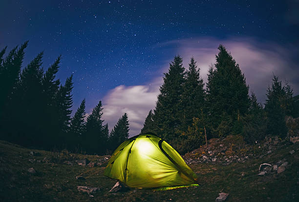 Illuminated  green  tent under stars at night  forest stock photo