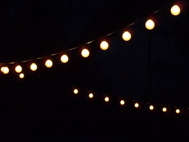 ilummination from strings of white bulb electric lights at night - ljusslinga bildbanksfoton och bilder