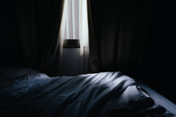 Image of a bedroom where light shines through the gaps in the curtains stock photo