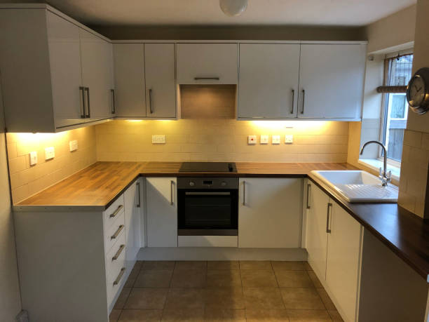 Image of empty rental property kitchen, magnolia painted walls, tiled flooring, oven, white cupboards with under lighting Stock photo showing empty rental property just after old tenant has moved out ready for new tenant to move in. below stock pictures, royalty-free photos & images