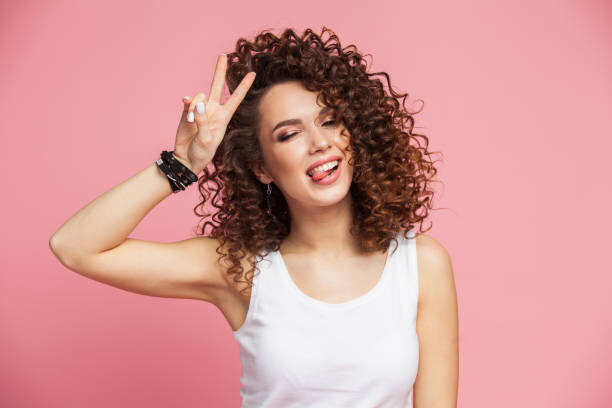 Image of happy young woman standing isolated over pink background showing peace gesture. Looking camera Image of happy young woman standing isolated over pink background showing peace gesture. Looking camera. curly hair stock pictures, royalty-free photos & images
