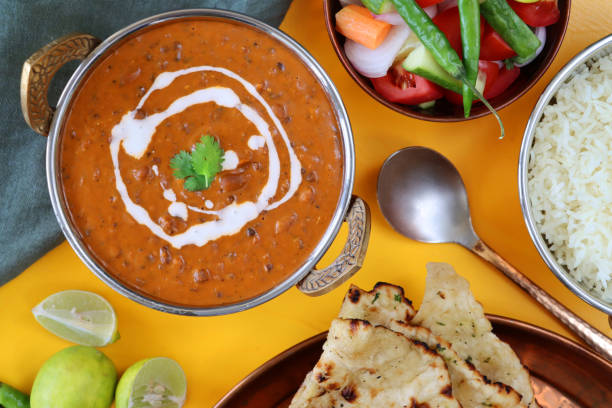 Image of metal kadhai-style serving bowls of homemade Dal makhani (black lentils and red kidney bean) curry recipe and white rice with side salad, naan flatbread, grey muslin, serving spoon, elevated view stock photo