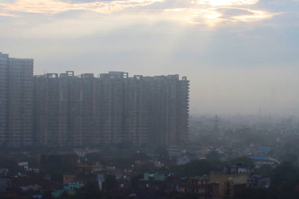 Image of sunlight breaking through clouds over cityscape view of New Delhi, Uttar Pradesh, India, Indian apartment block rooves surrounded by polluted foggy misty sky, hazy sky pollution caused by car fumes exhausts and factory emissions stock photo
