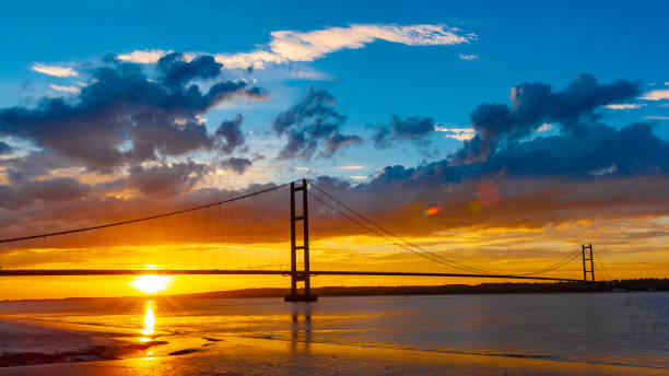 Image of the Humber Bridge at sunset seen from the mudflats at Barton on the south bank. An atmospheric sunset view of the Humber Bridge in the UK that joins Hessle in Yorkshire to Barton in Lincolnshire.  It was once the longest single span suspension bridge in the world. hull stock pictures, royalty-free photos & images