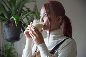 窓のそばで自家製ジューススムージーを飲む若い女性の画像写真