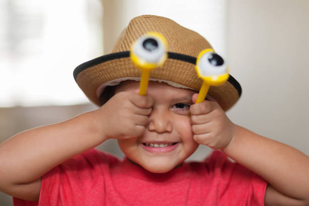 A imaginative latino boy having fun and playing with bug eyes, pretending to be insect, four years old and wearing a kids hat. stock photo