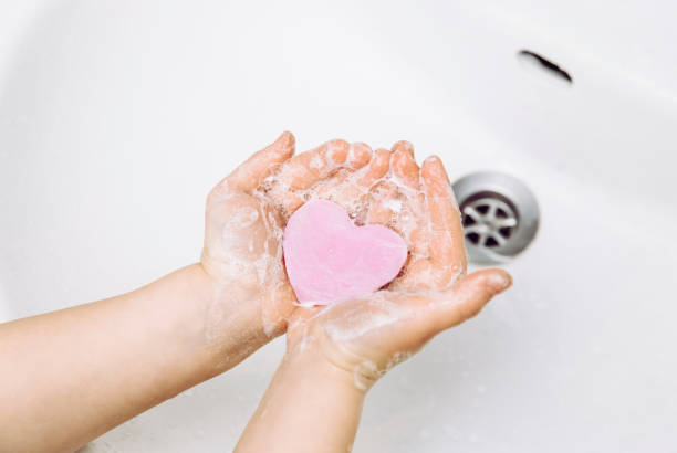 Importance of personal hygiene care. Flat lay view of child washing dirty hands with pink heart shape soap bar, lot of foam. Copy space. Importance of personal hygiene care. Flat lay view of child washing dirty hands with pink heart shape soap bar, lot of foam. Copy space. grooming product stock pictures, royalty-free photos & images