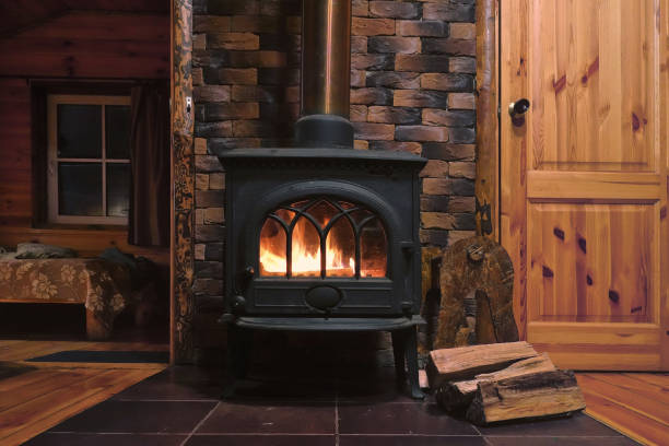 In a cast-iron furnace, a fire burns. There is wood near the stove. Fragment of the interior of a country house. The iron furnace is heated. There is wood near the stove. It's dark outside the window. firewood stock pictures, royalty-free photos & images