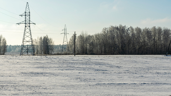 In background high-voltage electricity power pylon on snowy field with trees. High voltage poles on blue sky background. Industry.