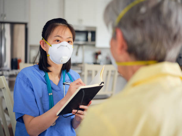 In Home Healthcare Worker with Senior Aged Woman A healthcare worker attends to a senior aged woman in a home. Both are wearing N95 protective masks. n95 mask stock pictures, royalty-free photos & images