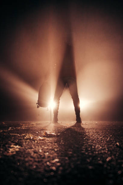 In the glare of car headlights, a man stands motionless, rushing with confidence and a backpack in one hand. Visual effect with different type of light. Sports photo at night. stock photo