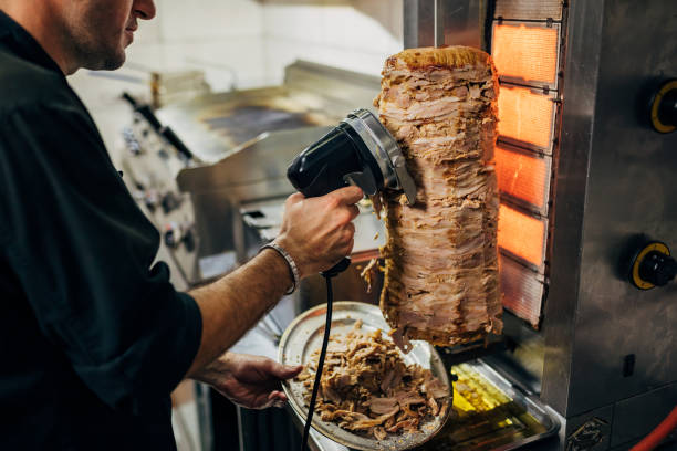 in the kitchen of the greek restaurant, the chef using the electric tool to cut the chicken gyros from the gyros grill - shoarma stockfoto's en -beelden