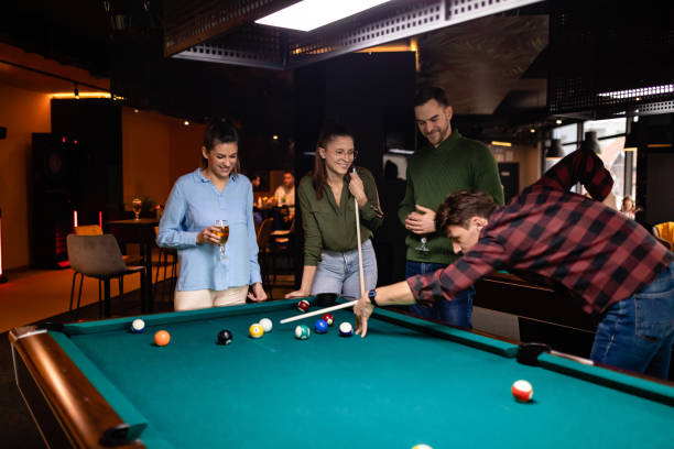 In the newly opened entertainment club, four smiling best friends play billiards and drink beer. stock photo