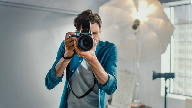 in de foto studio met professionele apparatuur: portret van de beroemde fotograaf met state of the art camera foto's maken met softboxes knipperen op de achtergrond. - photographer stockfoto's en -beelden