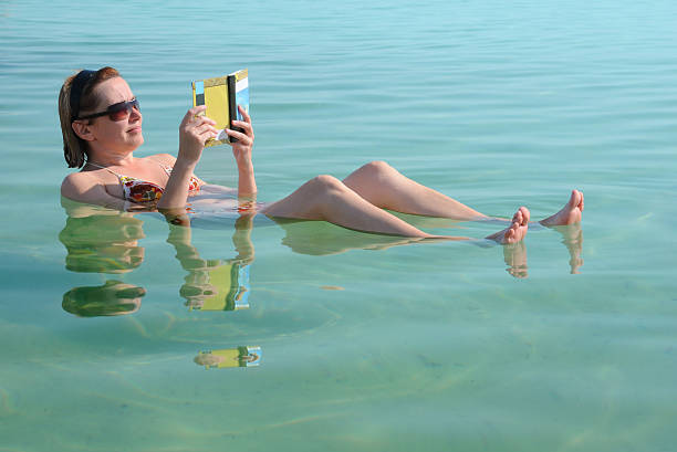 In the Waters of Dead Sea Caucasian woman reads a book floating in the waters of the Dead Sea in Israel floating on water photos stock pictures, royalty-free photos & images