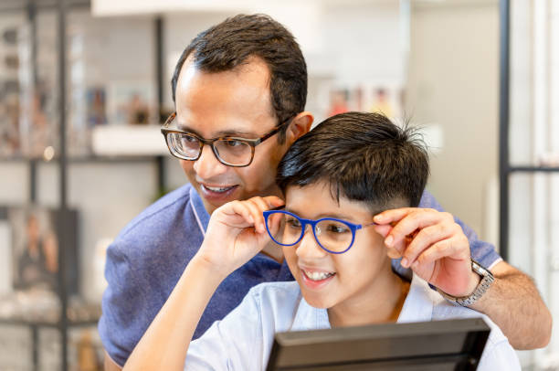 Indian father and son choosing eyeglasses in optics store stock photo