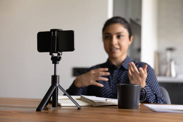 Indian female coach record vlog on smartphone Millennial Indian female vlogger or coach record video live broadcast on smartphone at home. Confident ethnic woman trainer or blogger shoot vlog or course on cell. Online communication concept. filming stock pictures, royalty-free photos & images