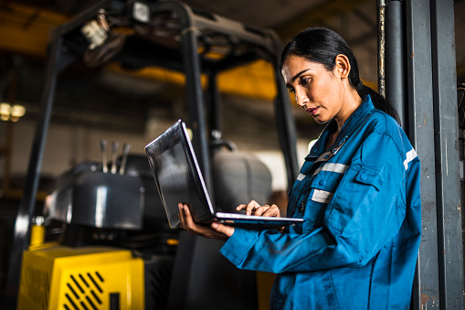 Indian Female Steel Factory Worker using a laptop in front of forklift