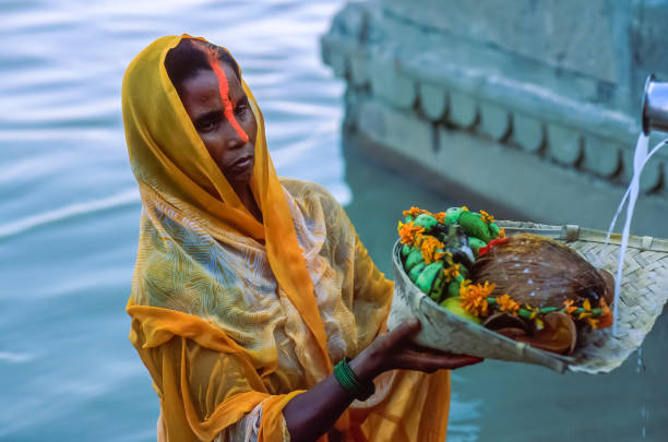 Indian Hindu woman devotee offering prayers to the Sun God during Chhath Puja in Varanasi A devout Hindu standing in the waters of the Ganga River, holds in her hands a basket with morning offerings for the Sun God, on the fourth day of the the Chhath Puja celebration, Varanasi, Uttar Pradesh, Northern India. chhath stock pictures, royalty-free photos & images