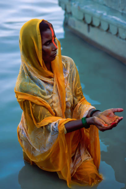 Indian Hindu woman devotee offering prayers to the Sun God during Chhath Puja in Varanasi, Uttar Pradesh, India. Devotee wearing an Indian women's garment standing in the waters of the Ganga River and holding her hands open as a prayer ritual on the fourth day of the celebration of Chhath Puja in Varanasi (India) chhath stock pictures, royalty-free photos & images