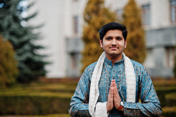 Indian man wear on traditional clothes Indian man wear on traditional clothes with white scarf posed outdoor against green bushes at park, show namaste hands sign. namaste greeting stock pictures, royalty-free photos & images