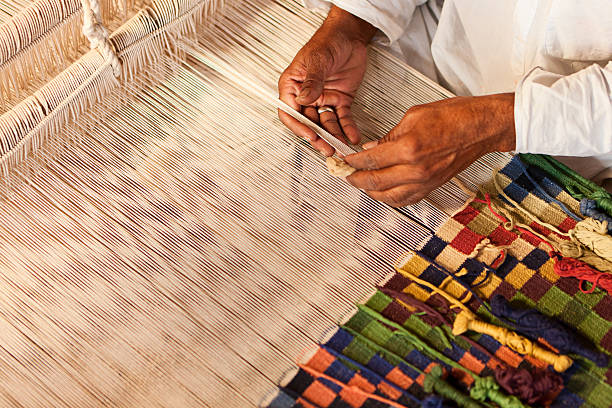 Homme indien tissant des textiles (durry). Village Salawas. Rajasthan. Homme indien tissant des durries. Le durry (tapis) est tissé en coton ou en laine. Les dessins géométriques sont produits par la technique de la tapisserie qui est un processus lent utilisant des bobines ou des papillons séparés pour chaque couleur sur toute la largeur s'emboîtant avec le fil coloré adjacent. Cette ancienne forme de tissage à la mode est très populaire au Rajasthan, en particulier dans le village de Salawas près de Jodhpur. http://bem.2be.pl/IS/rajasthan_380.jpg photos et images de tapis