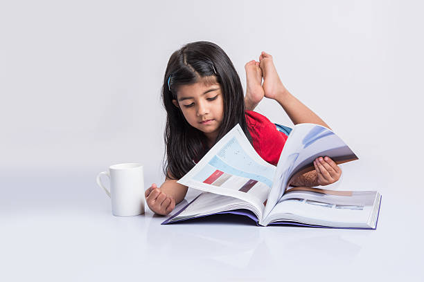indian small girl child reading book on ground indian small girl reading book, asian girl child reading book over white background, cute 5 year old indian small girl reading book with milk mug kids learn books stock pictures, royalty-free photos & images