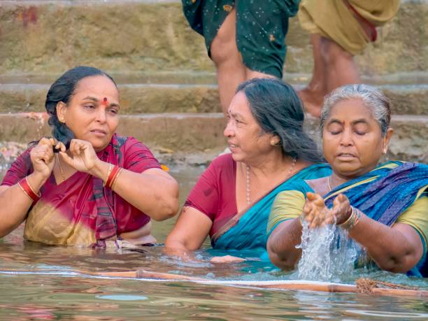 Indian women bathing in the Ganges River in Varanasi, India. Varanasi, India - November 14, 2015. Three Indian women bathe in the Ganges River, as part of a Hindu religious pilgrimage during the annual Diwali Festival. They are fully clothed in their traditional colorful saris in water that has pollution issues. ganges river stock pictures, royalty-free photos & images