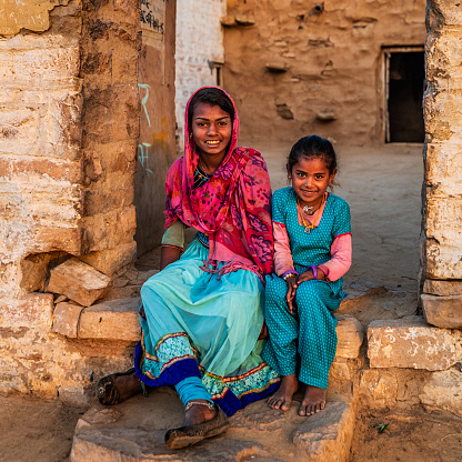 Indian young girls sitting next to their house in desert village, Rajasthan, India.