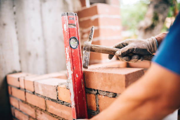 industrial worker building exterior walls, using hammer and level for laying bricks in cement. Detail of worker with tools stock photo