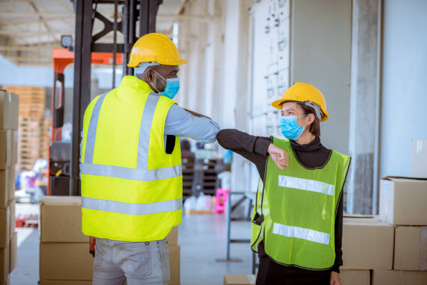 논의 중인 업계 종사자들은 공장 창고에서 새로운 정상 개념에 인사, 그들은 바이러스를 보호하기위해 안전 균일 하드 모자와 의료 마스크를 착용 - 직업 안전 보건 뉴스 사진 이미지
