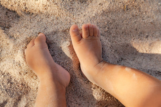 Infant baby feet on sandy beach as a background, childhood and vacation concept stock photo