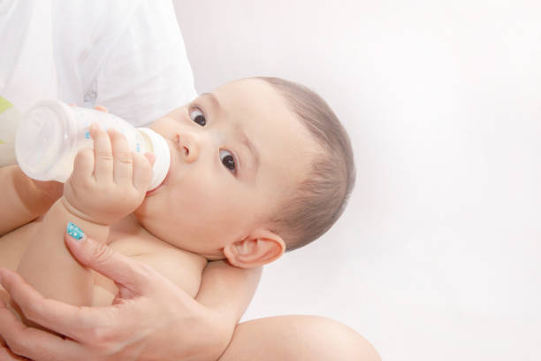 niños de 7-8 meses de edad están bebiendo leche de la botella. por las manos de la madre. - baby formula fotografías e imágenes de stock