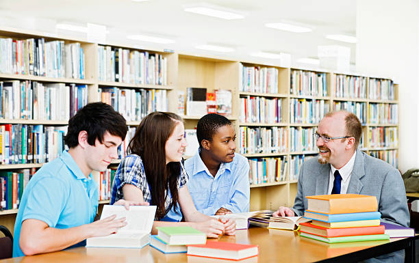 Informal seminar with three students and teacher in library stock photo