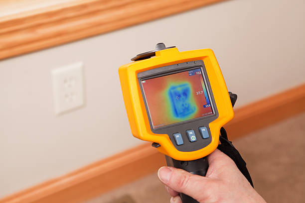 Infrared Thermal Imaging Camera Pointing to Wall Outlet An infrared thermal imaging system being used during a home energy audit. The camera is pointed to a wall outlet, on an exterior wall, showing the blue (cold) area within the home’s insulation. The center target area reads 37.7 degrees with a range of 33 to 59 degrees in the area.  Energy audits are performed to determine how efficient the house is and to suggest steps to increase energy efficiency. infrared stock pictures, royalty-free photos & images