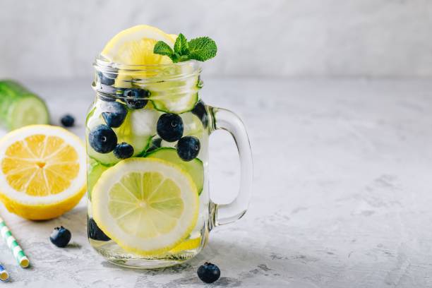 Infused detox water with lemon and cucumber slices, blueberry and mint. Ice cold summer lemonade in glass mason jar stock photo