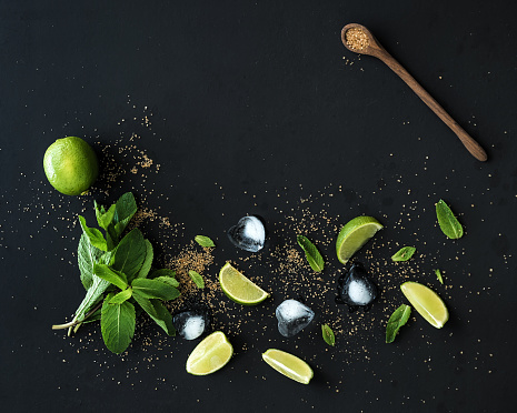 Ingredients for mojito. Fresh mint, limes, ice, sugar over black backdrop. Top view