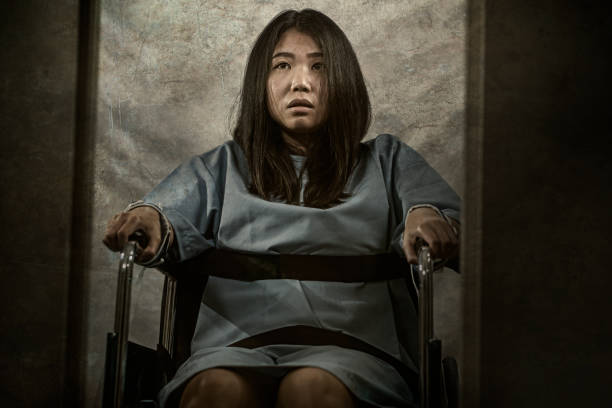 insanity asylum horror movie style portrait of young sick and psychotic Asian Chinese woman isolated and locked in mental hospital security cell sitting on wheelchair suffering schizophrenia insanity asylum horror movie style portrait of young sick and psychotic Asian Chinese woman isolated and locked in mental hospital security cell sitting on wheelchair suffering schizophrenia restraining stock pictures, royalty-free photos & images