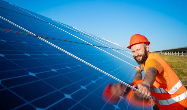 Installing of stand-alone solar photo voltaic panel system. Technician in hard-hat, mounting big shiny solar module  on green summer view background. Alternative energy concept. stock photo