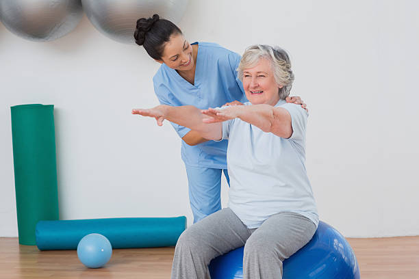 instructor assisting senior woman in exercising - fysiotherapie stockfoto's en -beelden