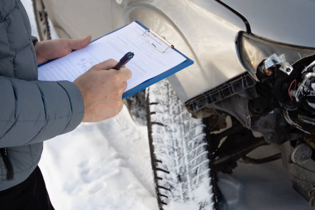 Insurance agent checking car after car accident and filling accident details form. Winter time. Focus on hands. stock photo
