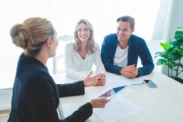 Insurance agent with couple looking through documents. Insurance agent with couple looking through documents. The agent is holding a digital tablet. Couple are casually dressed. They sitting at a table at home and are looking a little happy and smiling. Investment Banker stock pictures, royalty-free photos & images