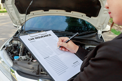 Insurance Agent Writing On Clipboard And Examining Car After Accident