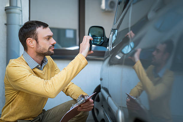Insurance expert at work Insurance agent inspects a car after accident. He is doing photograph of damage.  car photos stock pictures, royalty-free photos & images